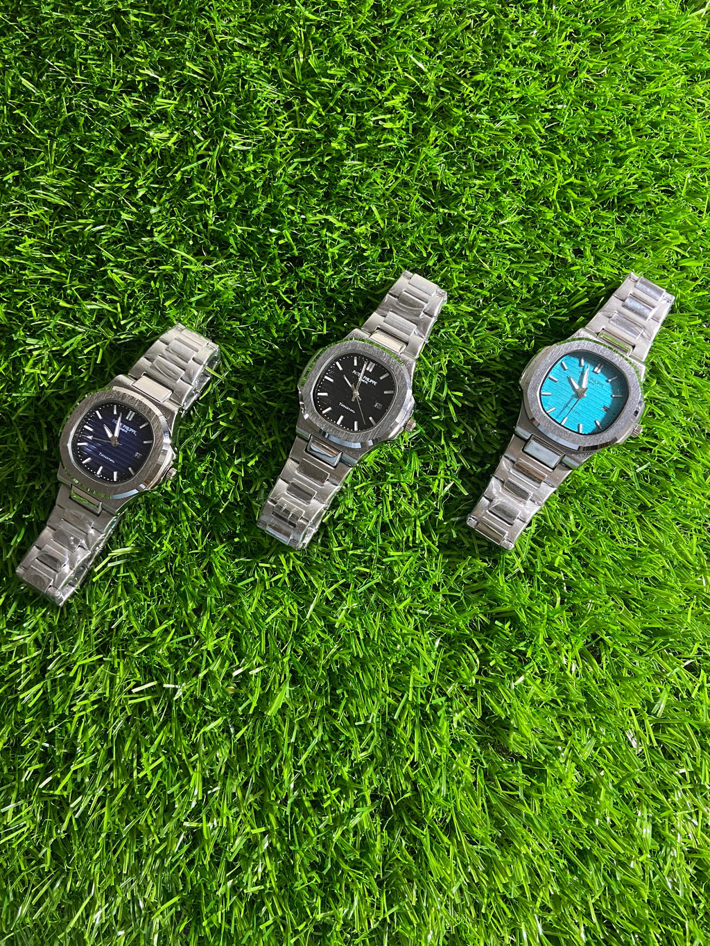 Three metallic watches on a grassy surface