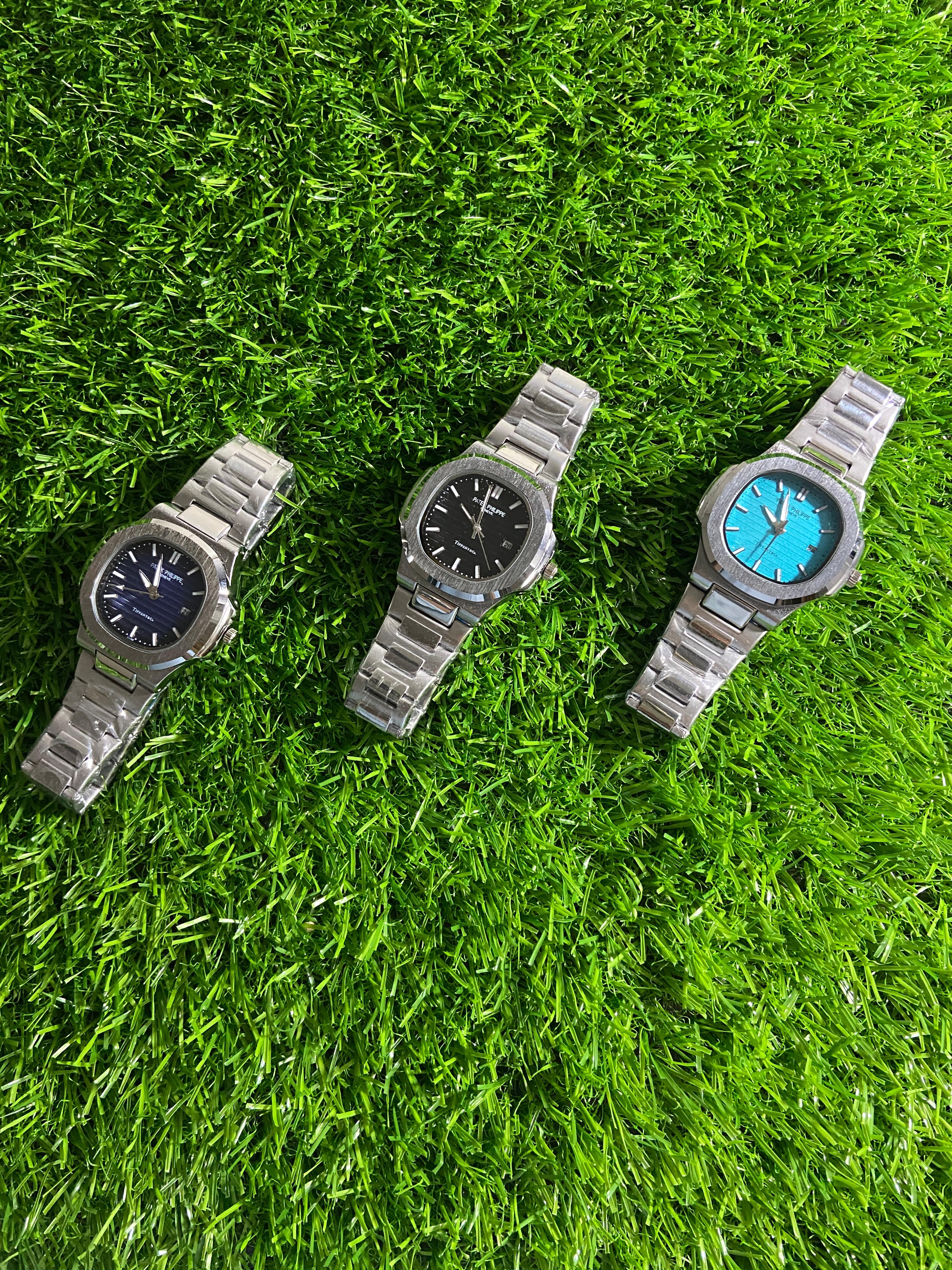 Three metallic watches on a grassy surface